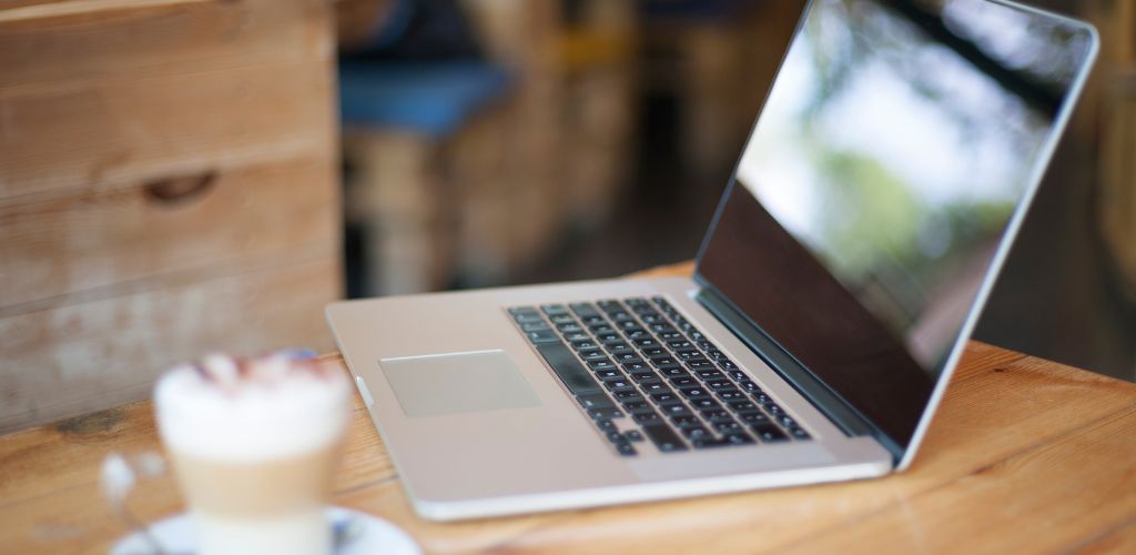 laptop in a cafe/coworking setting with latte on desk 