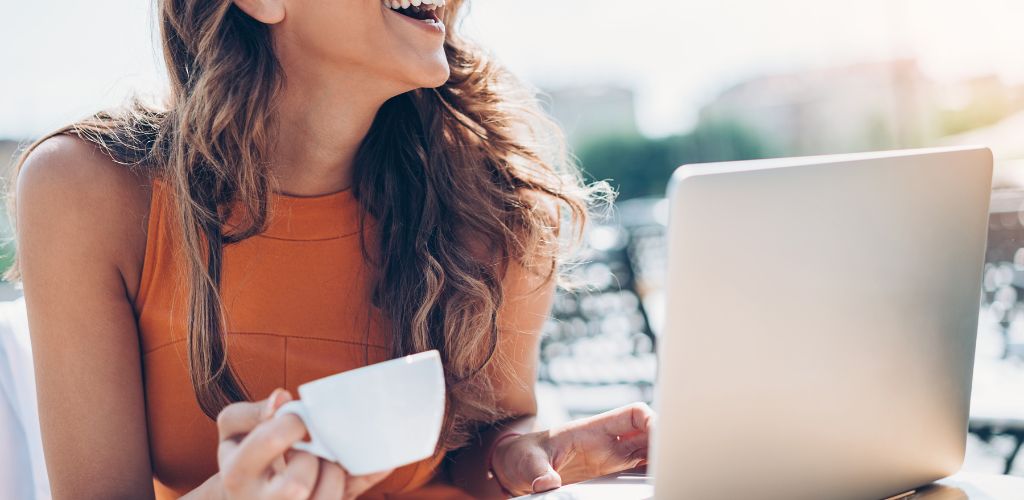 smiling digital nomad with laptop and coffee cup laughing outside